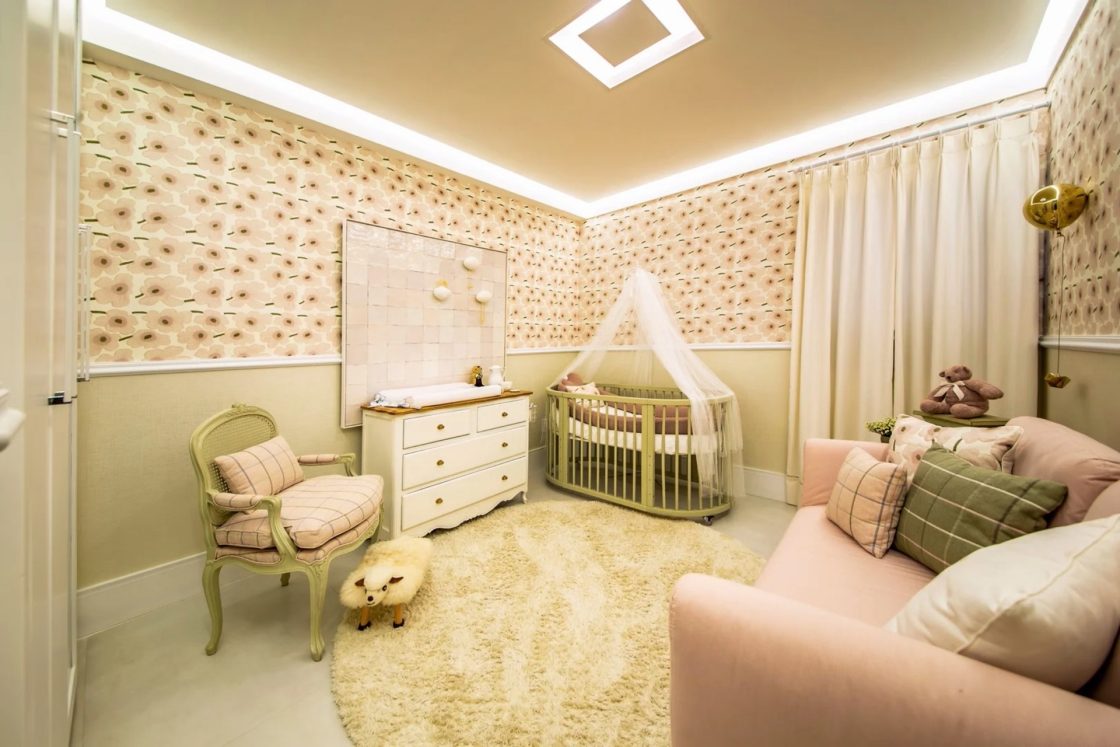 Quarto de bebê com papel de parede estampado, paredes esverdeadas e móveis como cadeira de amamentação, cômoda e berço