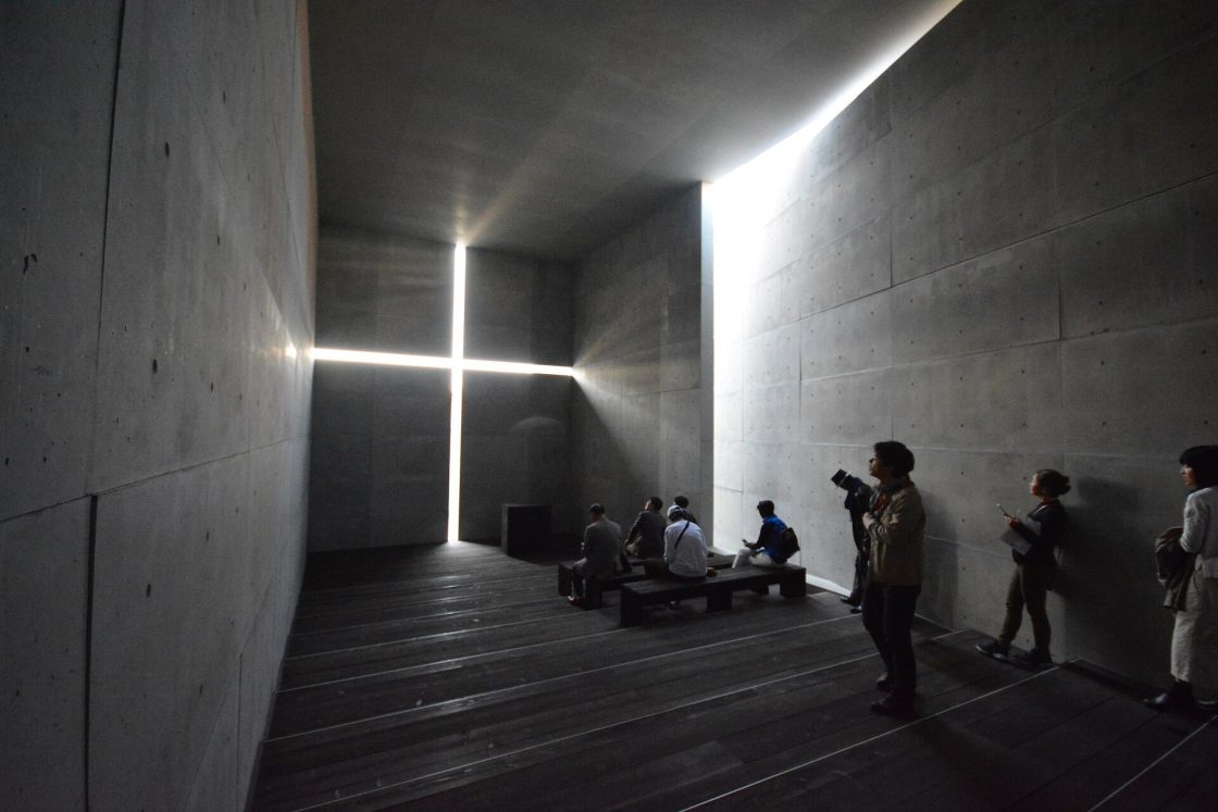 Foto da Igreja da Luz, de Tadao Ando. Construção em concreto com um grande recorte em formato de cruz, por onde entra luz natural. Osaka, Japão.