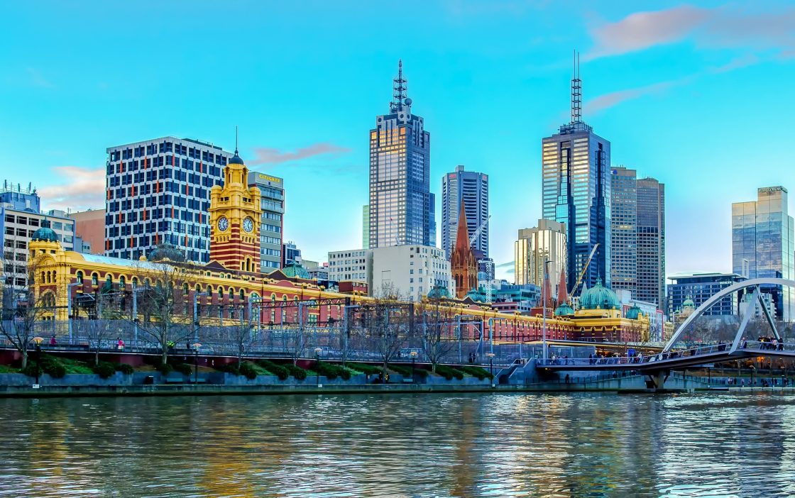 Vista da cidade de Melbourne, na Austrália, às margens do rio Yarra. Há prédios e outras construções.