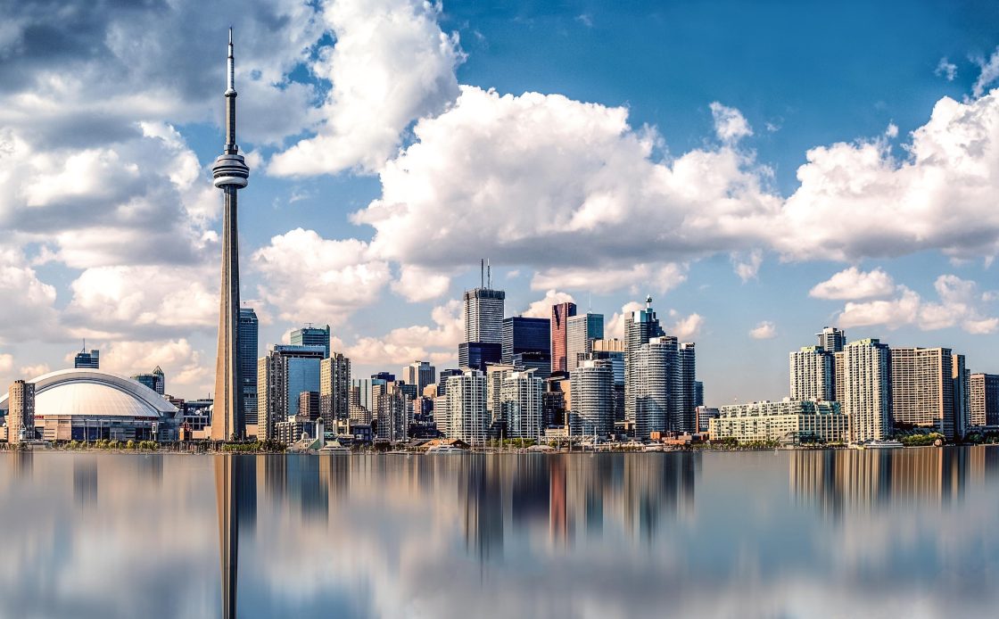 Vista aérea de Toronto, com destaque para a CN Tower, uma torre de televisão com mirante. Ao fundo do lago Ontário, há edificações