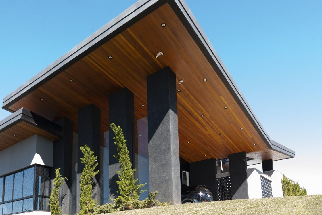 Casa com telhado invertido, formando um "V" revestido de madeira na parte de dentro, com colunas em preto que dão sustentação