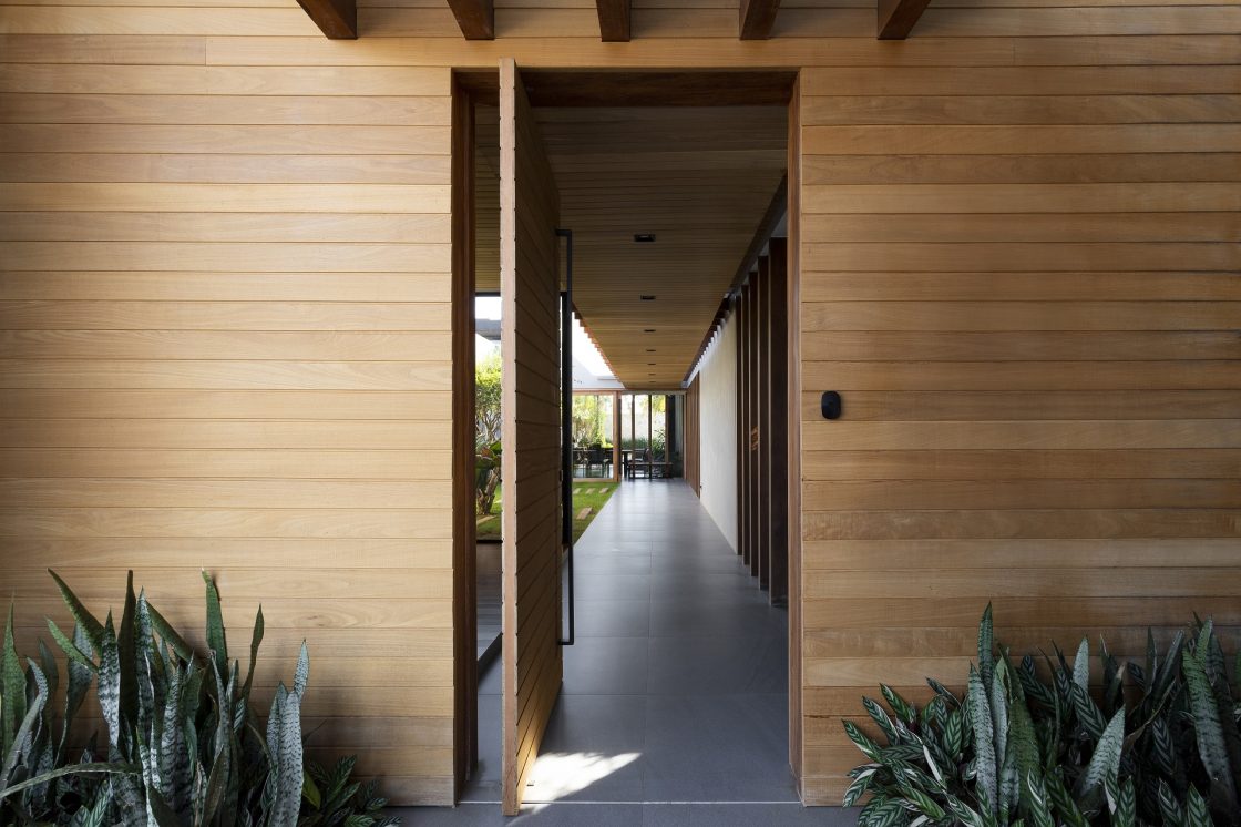 Detalhe de entrada de casa com revestimento em madeira e porta pivotante no mesmo material