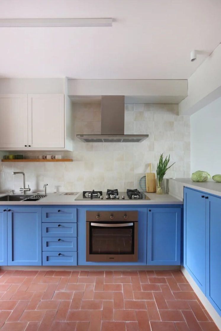 Cozinha azul com bancadas e azulejos claros. Há uma coifa com acabamento metalizado