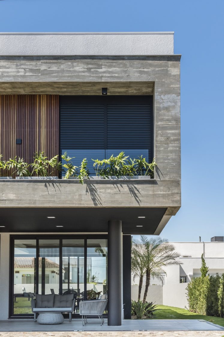 Imagem com foco no segundo pavimento de casa contemporânea, que mistura concreto aparente com detalhes em madeira e vidro