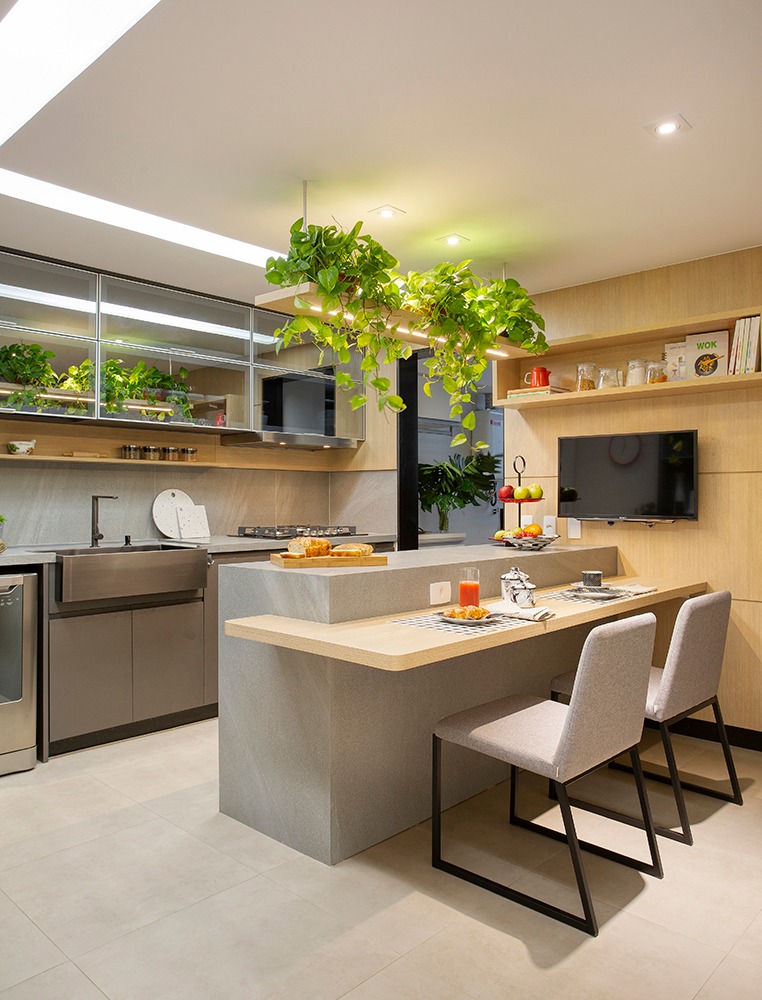 Cozinha com bancada de apoio e para refeições, superfícies revestidas de porcelanato e madeira, plantas decorativas