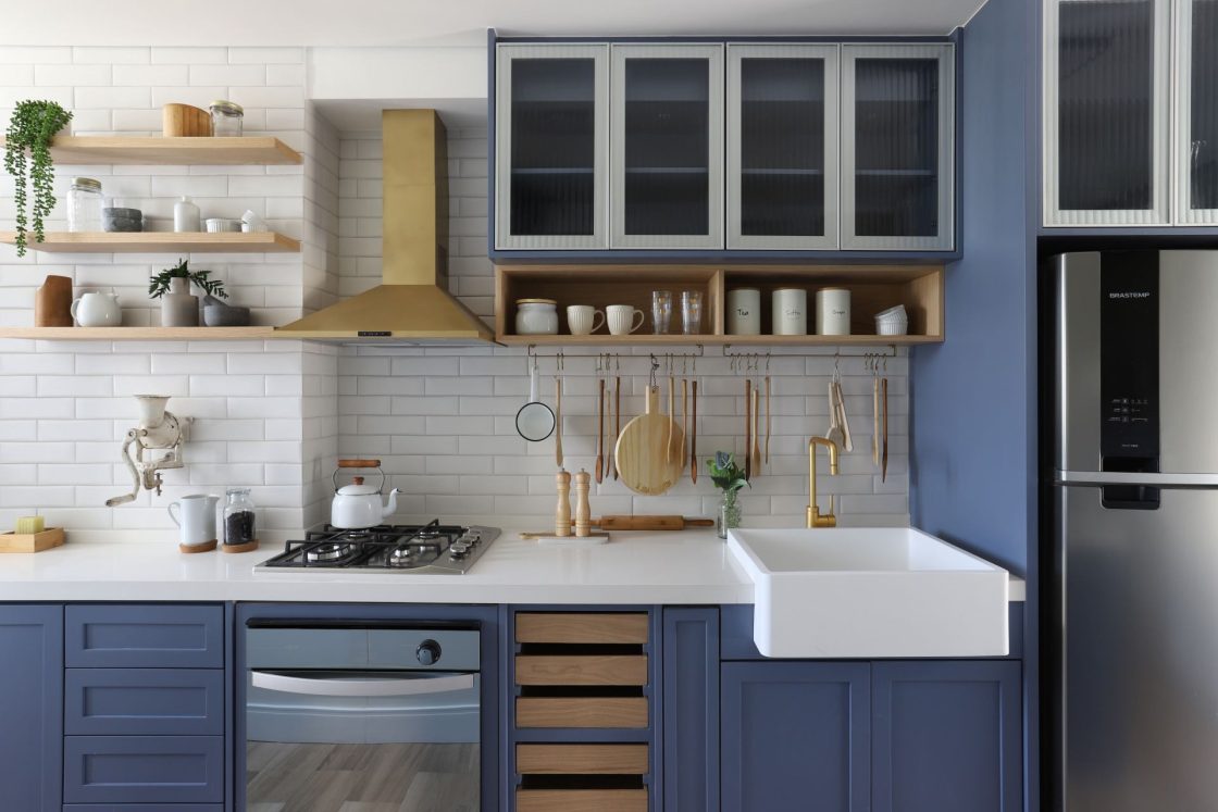 Cozinha com revestimento e bancada brancos, armários azuis e utensílios pendurados