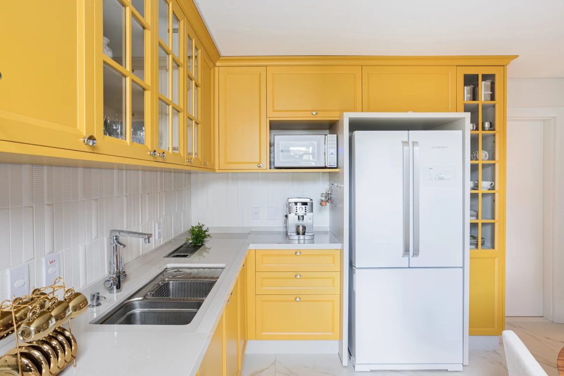 Cozinha com armários amarelos, bancada branca e eletrodomésticos claros