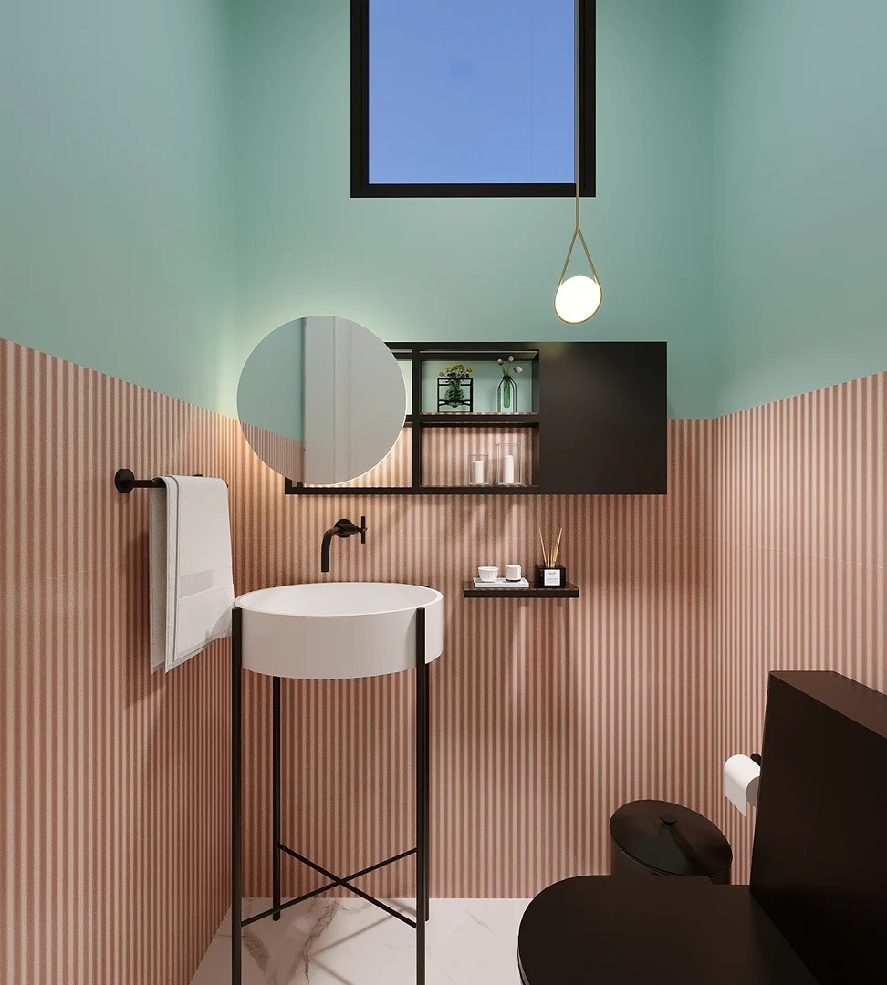 Banheiro com revestimento meia-parede, azul em cima e rosa embaixo. O sanitário é preto, assinm como uma estante na parede. A pia é branca e há um espelho redondo na parede.