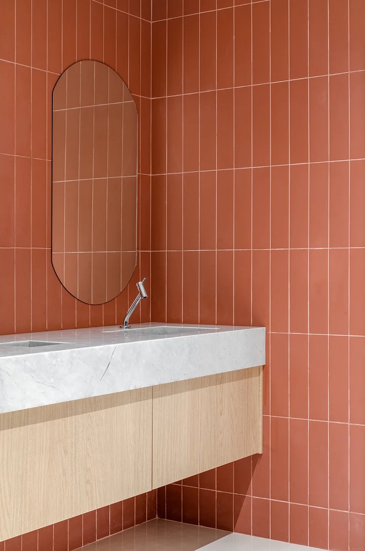 Banheiro com azulejos estilo subway em terracota, espelho ovalado e armário em madeira