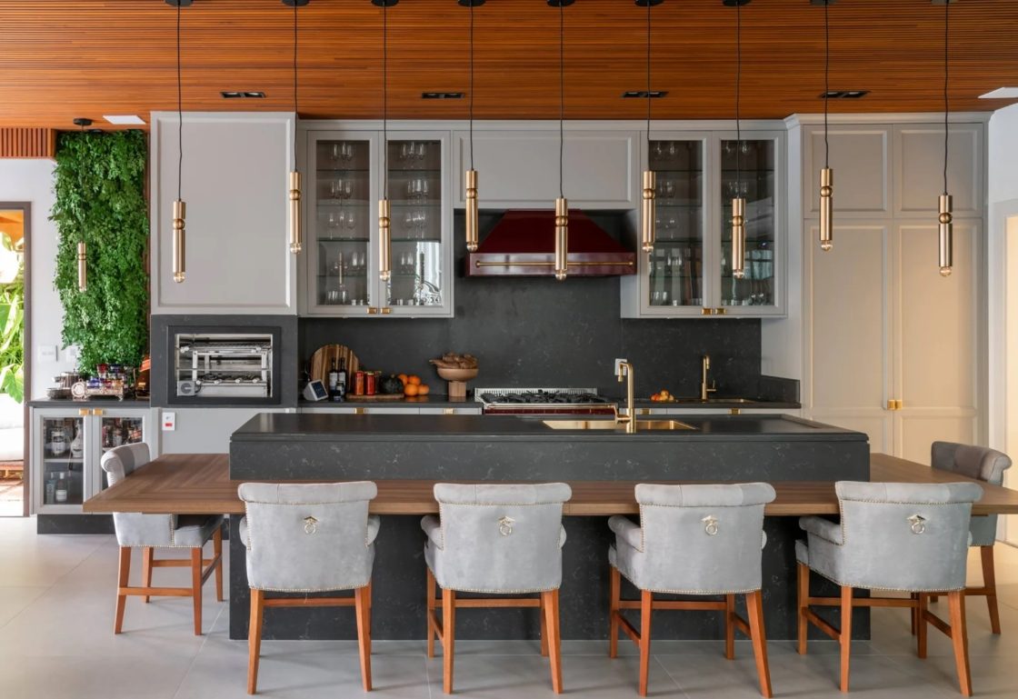 Cozinha com armários claros, ilha com mesa em madeira embutida e cadeiras em estilo clássico em cinza