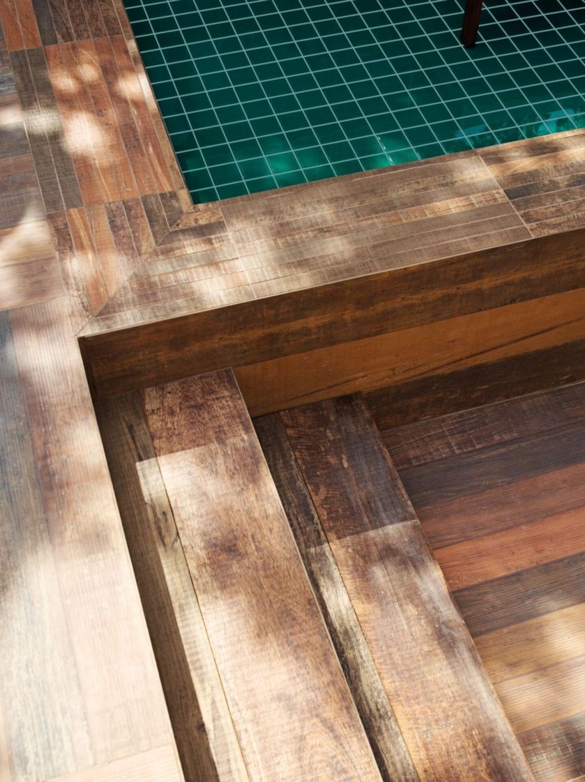 Detalhe da lateral de uma piscina com revestimento esverdeado e, na lateral, porcelanato que reproduz madeira