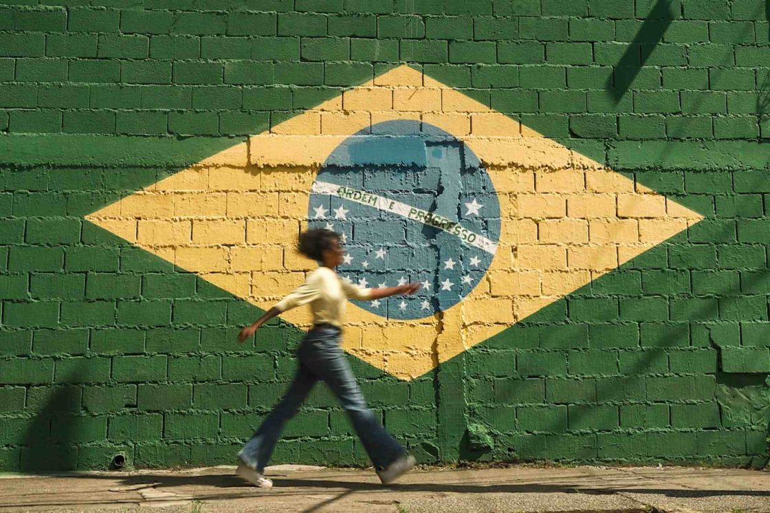 Mulher passando em frente a um muro que está pintado com a bandeira do Brasil