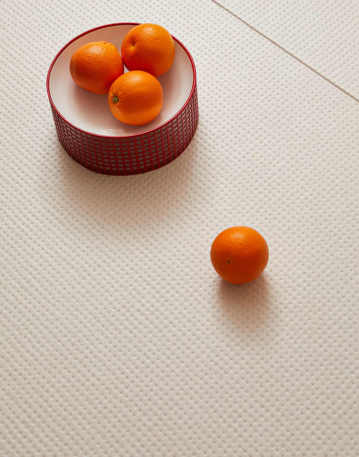 Revestimento com fundo claro e pequenos pontos aprofundados, com pingos em vermelho. Há uma cesta com laranjas sobre ele