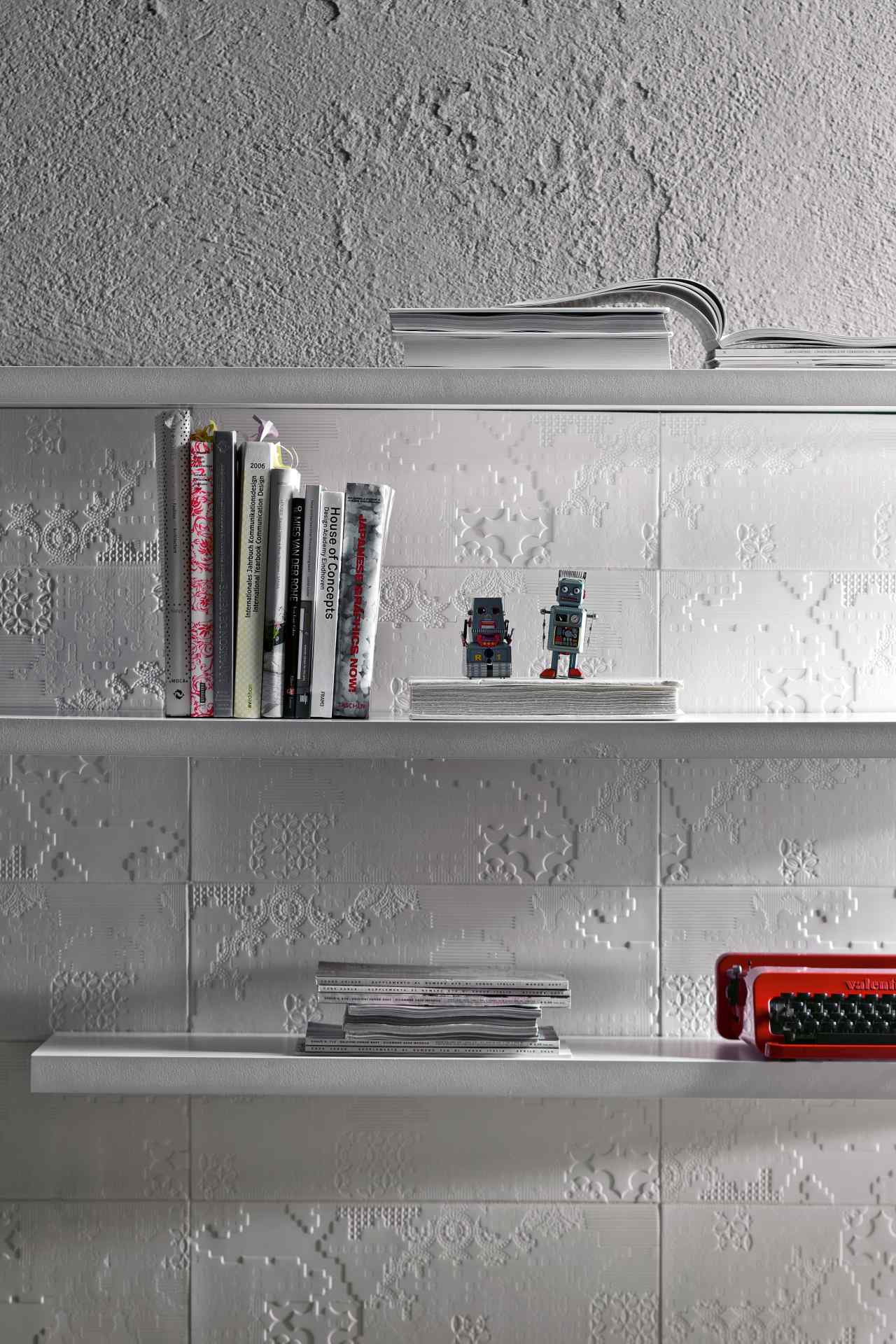 Bas-Relief Patchwork Bianco aplicado em uma parede, atrás de prateleiras com livros e outros objetos
