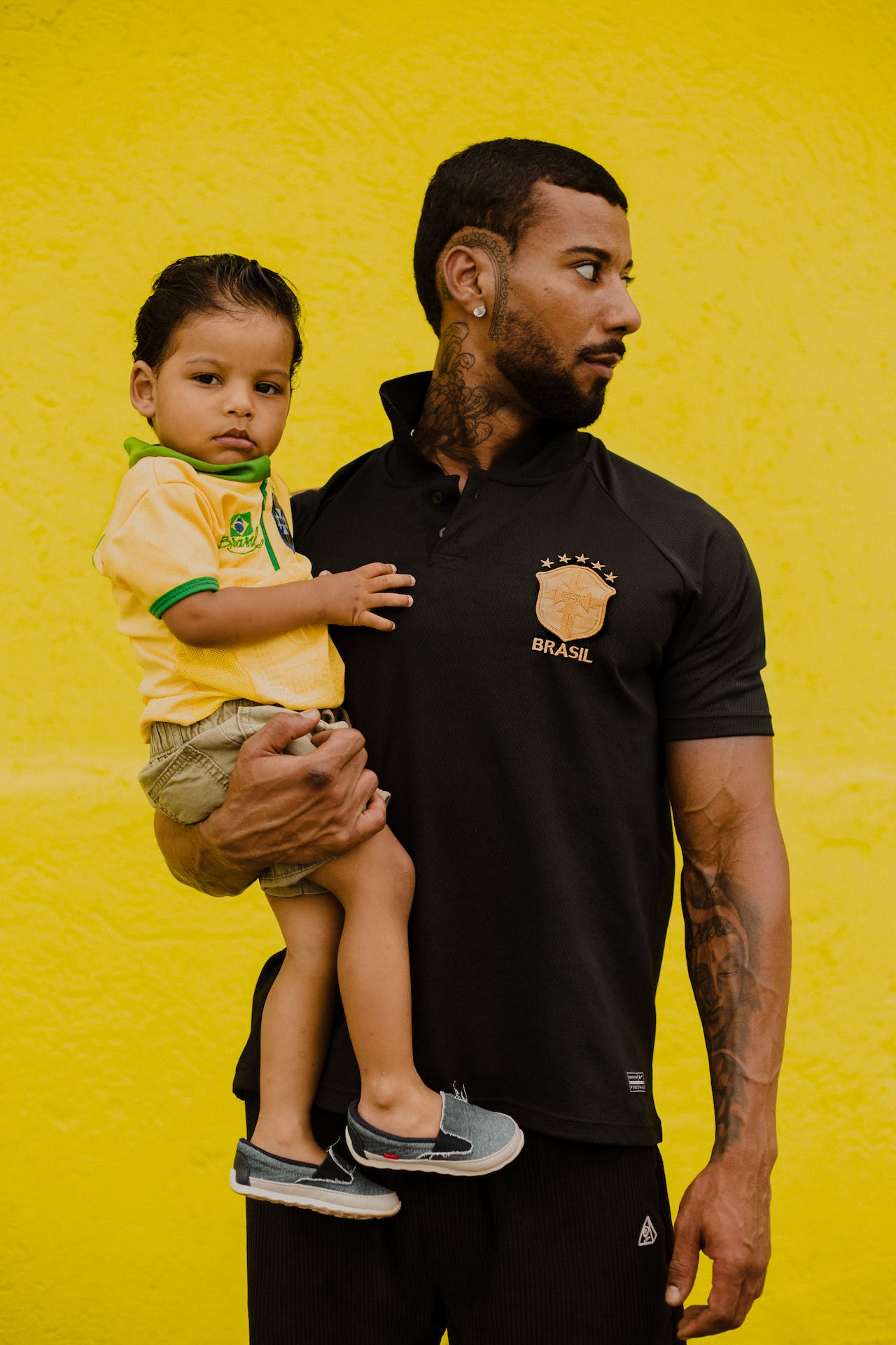Pai segurando filho no colo. Ambos usam camisas da Seleção Brasileira de Futebol