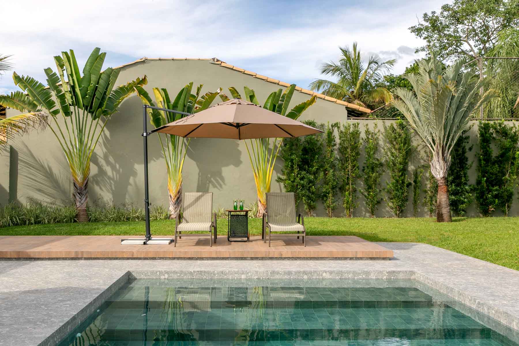 Área externa com piscina e jardim com ombrelone  eespreguiçadeiras. Porcelanato cinza na piscina e bordas sobreposto por porcelanato terracotta na área das espreguiçadeiras