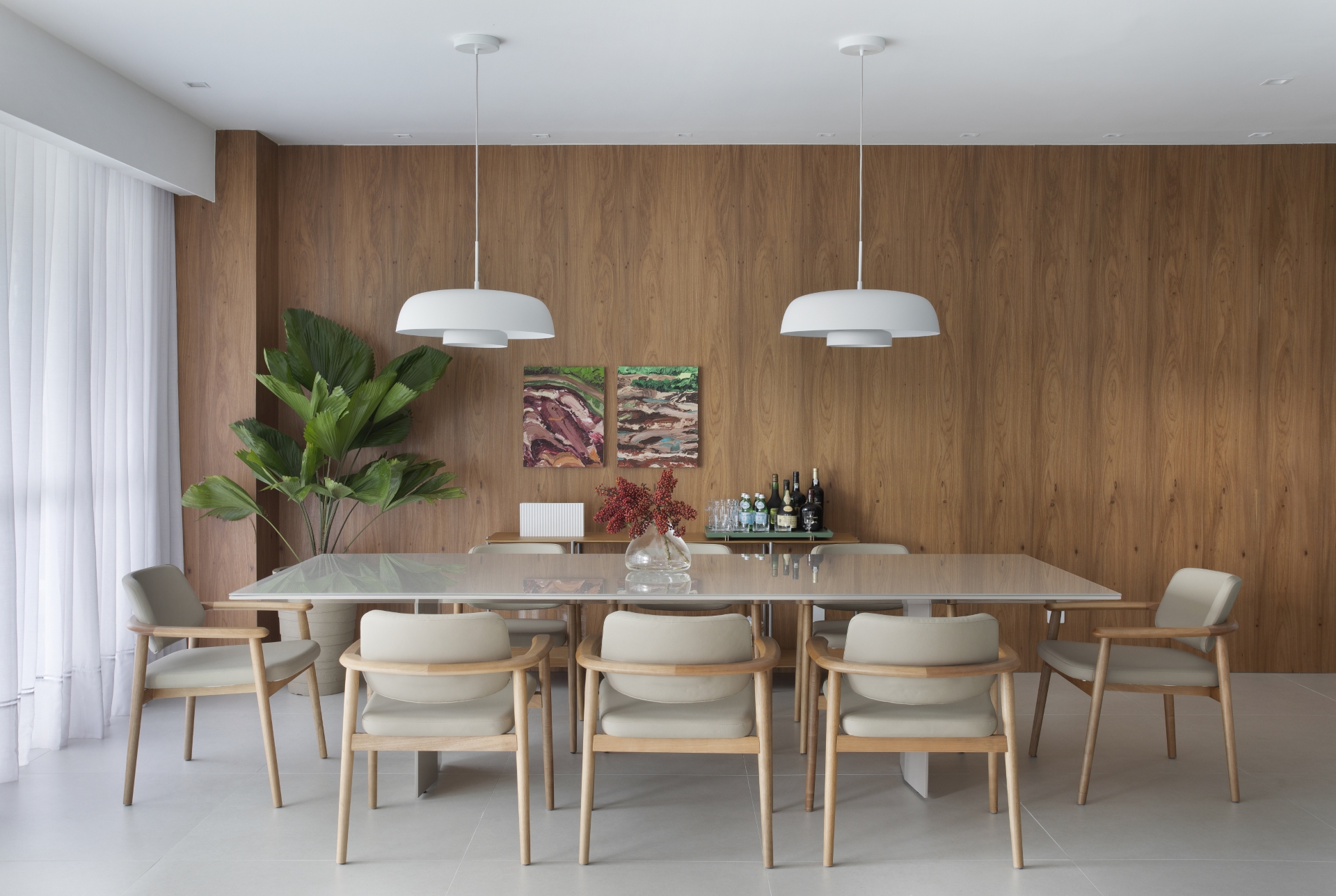 Sala de jantar com mesa em porcelanato, paredes com porcelanato com textura de madeira, dois pendentes, cortinas claras e vaso com planta próximo da parede