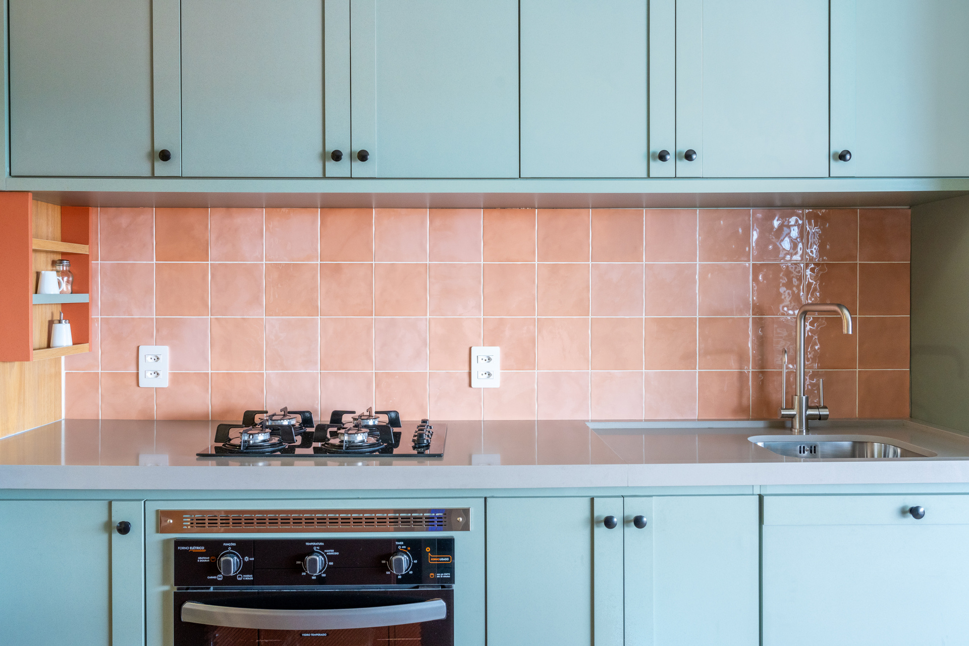 Cozinha com revestimento em cor pêssego na parede, armários em azul e eletrodomésticos pretos