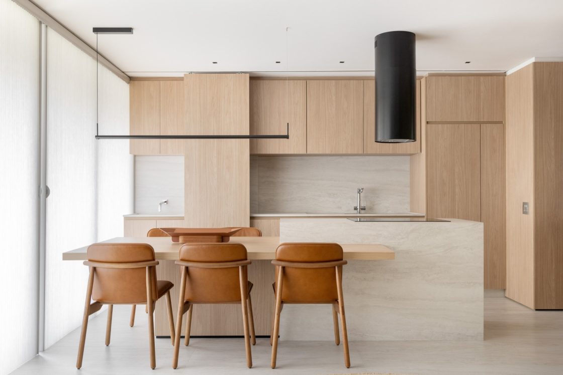 Cozinha em tons claros e quentes, com ilha revestida com porcelanato travertino