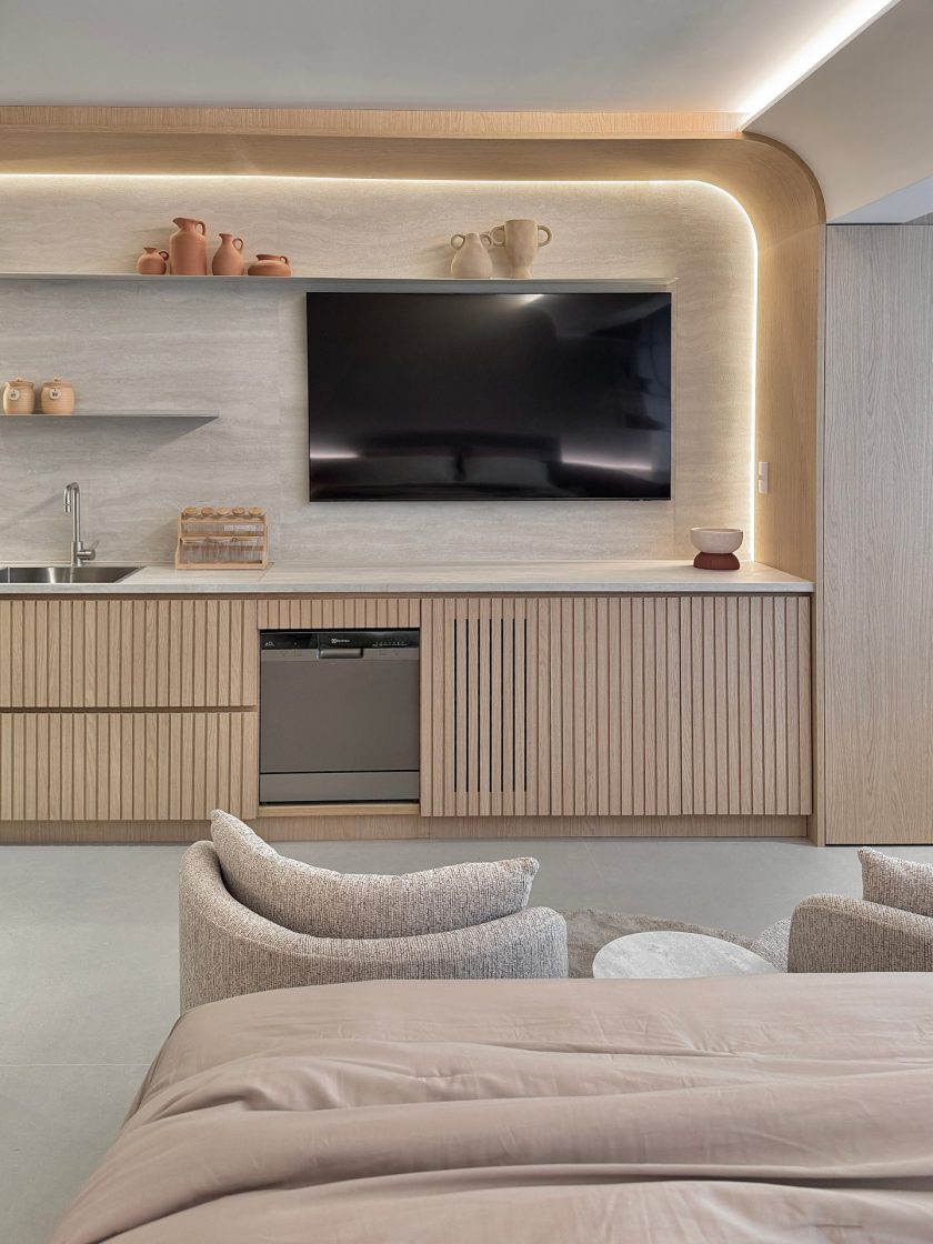 Bancada ripada com televisão fixada na parede em fundo de porcelanato travertino que forma painel