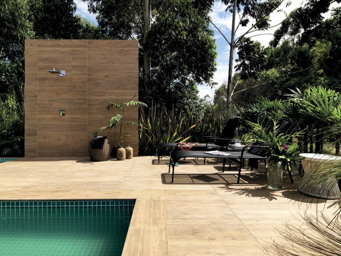 Área externa com piscina, espreguiçadeiras, plantas e uma parede com revestimento e uma ducha