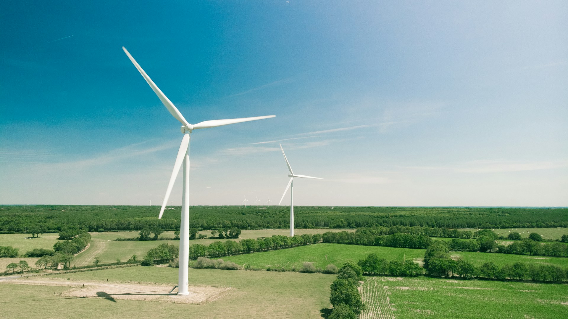 Turbinas de geração de energia eólica em paisagem verde, céu azul