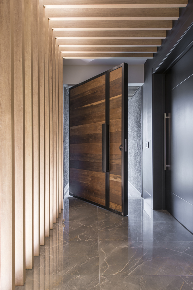 Hall de entrada com piso em mármore marrom, porta pivotante de madeira e painel ripado