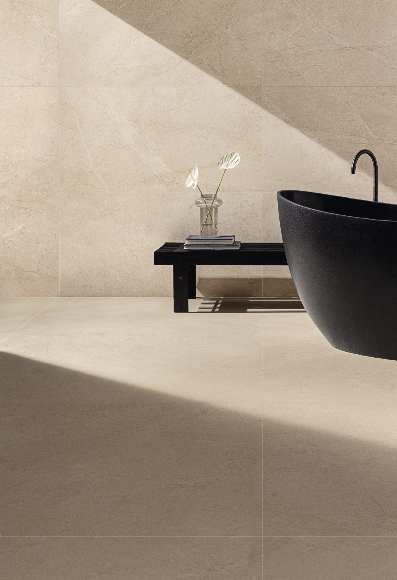Banheiro amplo com piso e parede em mármore bege. Há uma banheira e um banquinho pretos