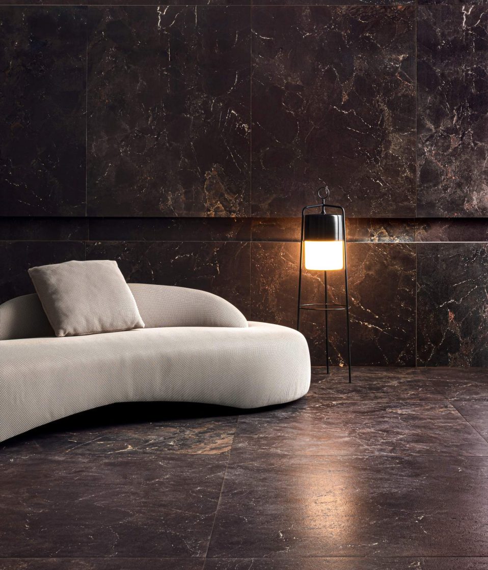 Living todo revestido com porcelanato marmorizado preto, com sofá orgânico bege-claro e luminária de piso ao lado