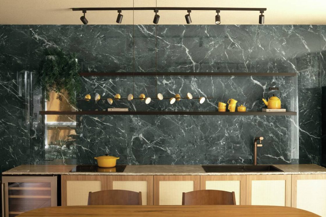Cozinha em conceito aberto com painel em porcelanato que reproduz mármore verde