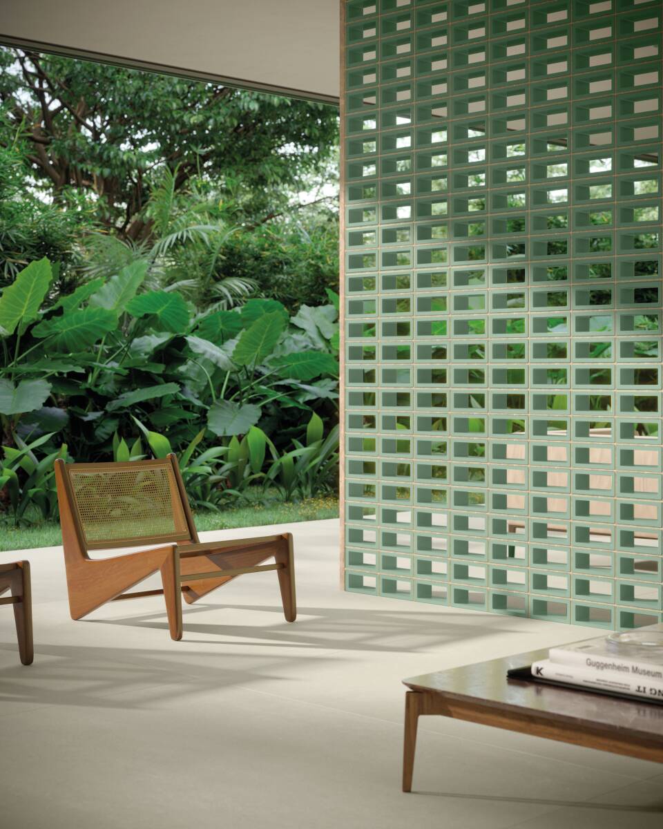Detalhe de ambiente externo com cobogó verde, cadeiras e vegetação