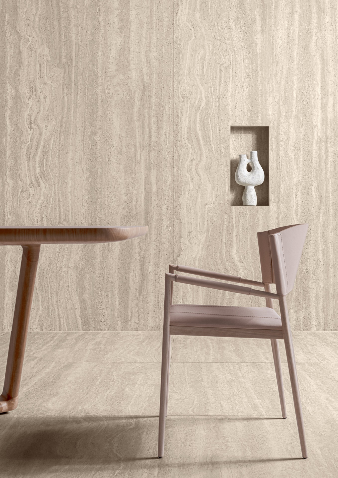 Detalhe de ambiente com piso e parede em revestimento que reproduz travertino. Há uma mesa, uma cadeira e uma escultura