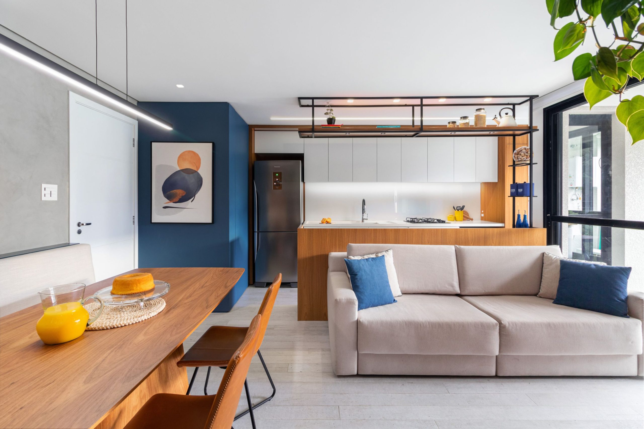 Apartamento com salas e cozinha integrada traz a cor azul em destaque.