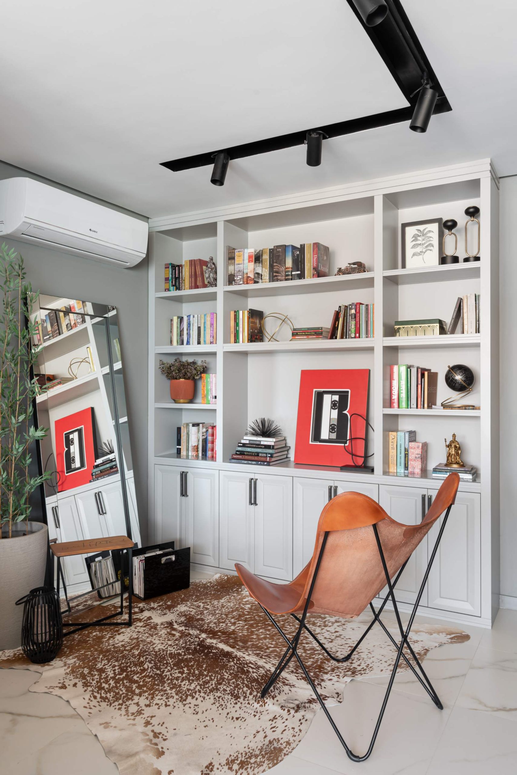 Ambiente para leitura com cadeira, estante com livros e objetos de decoração.