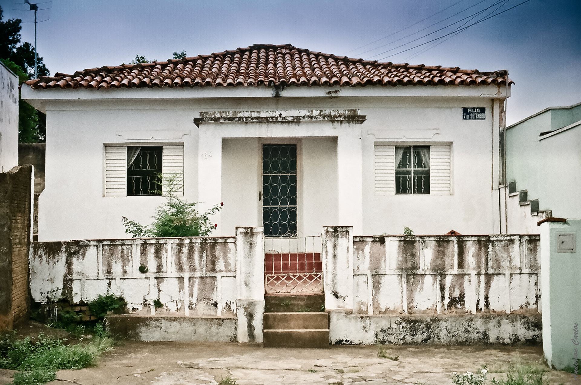 Casa de um pavimento na cor branca, com muro baixo e telhado colonial