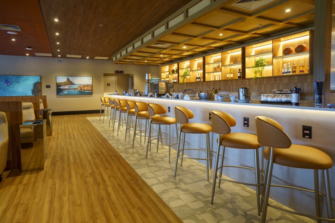 Bar de restaurante com luzes indiretas e baixas, piso amadeirado e piso decorado sob as banquetas em tom de marrom