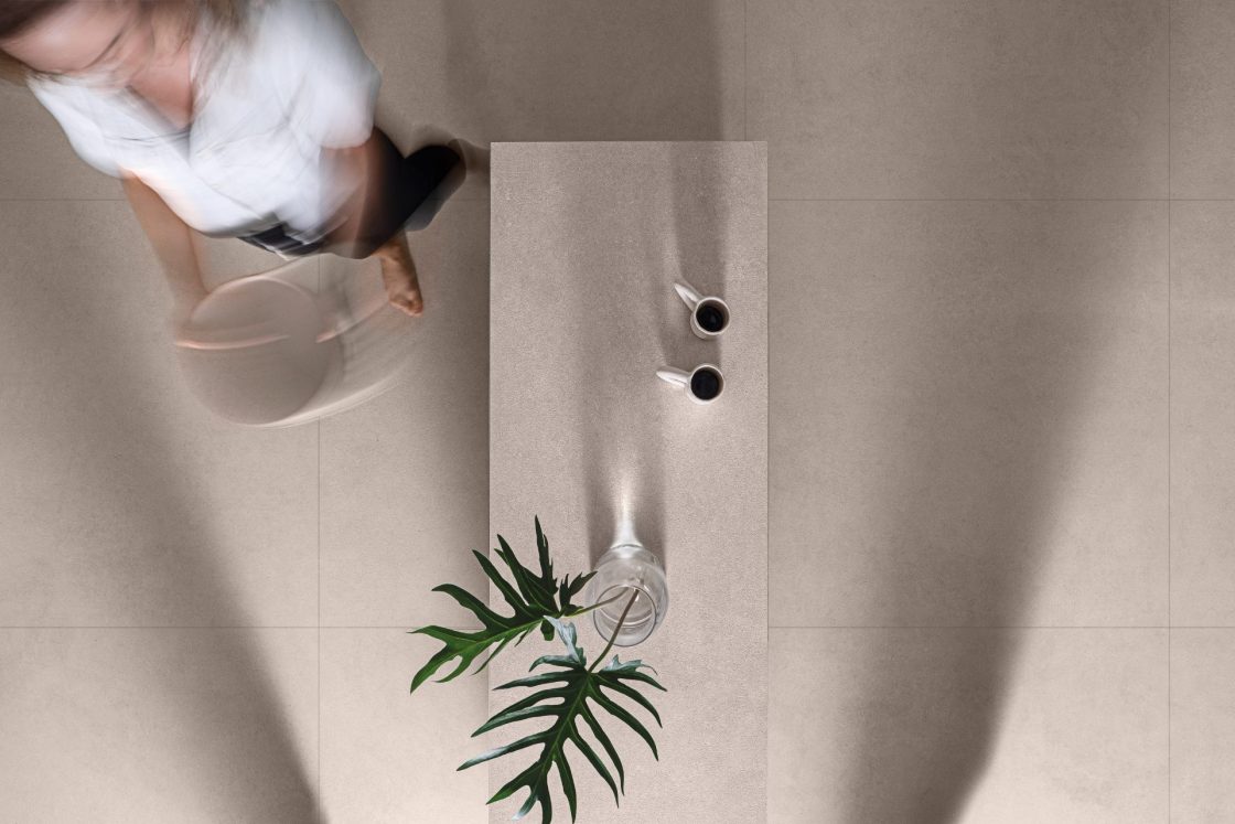 Mulher segurando vasilha ao lado de bancada revestida com porcelanato que reproduz pedra