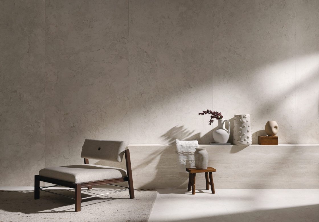 Ambiente com revestimento que reproduz travertino, com poltrona, bancada com vasos decorativos e banco de madeira, também com vaso em cima