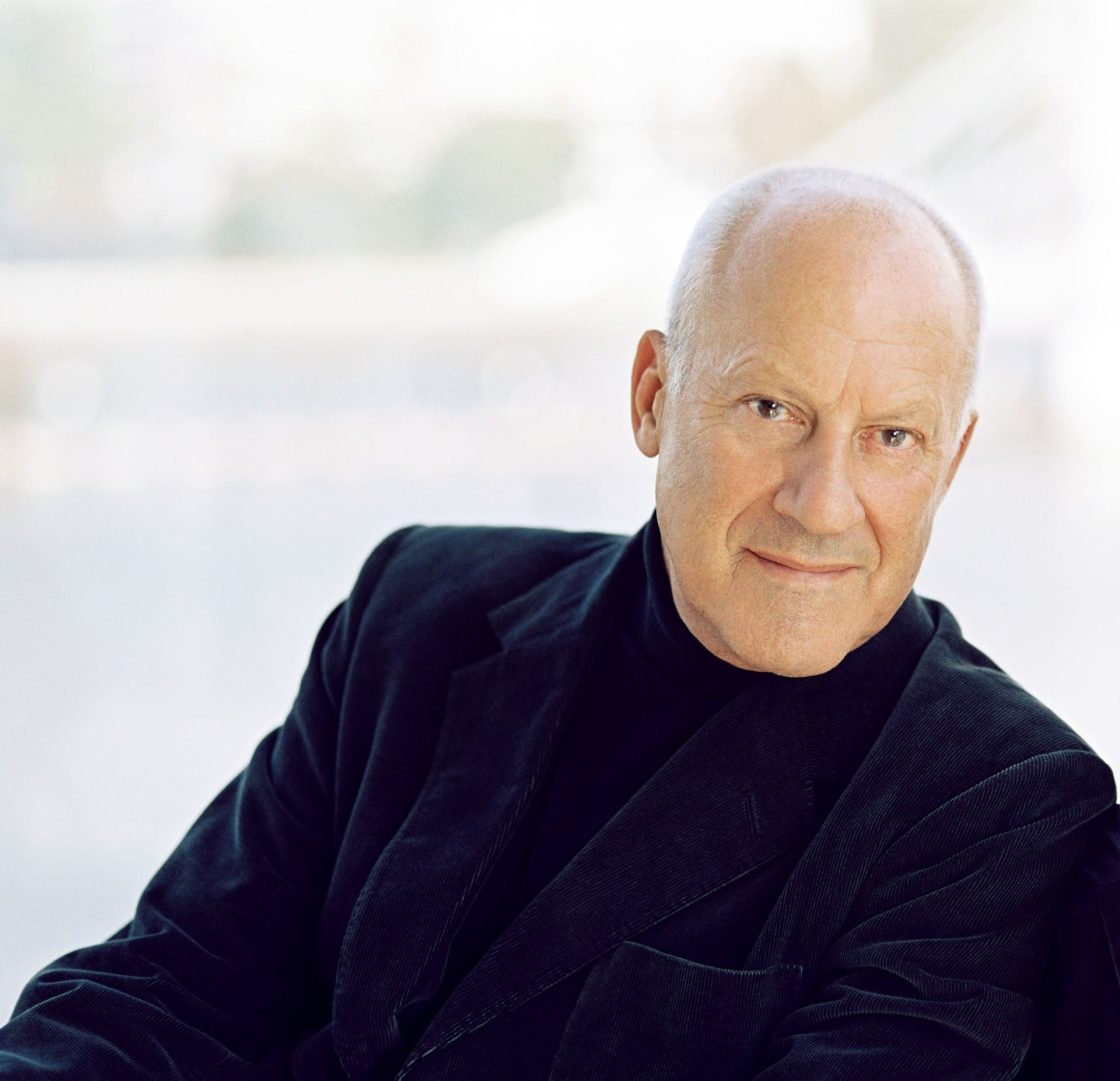 Retrato de Norman Foster em pose descontraída, olhando para a câmera, destacando o arquiteto britânico