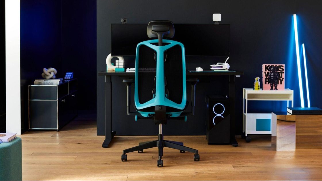  Fotografia de um espaço interno com um setup gamer que inclui uma cadeira ergonômica Vantum na cor preta e azul, uma mesa preta e um computador gamer com dois monitores, além de itens de escritório e decoração.