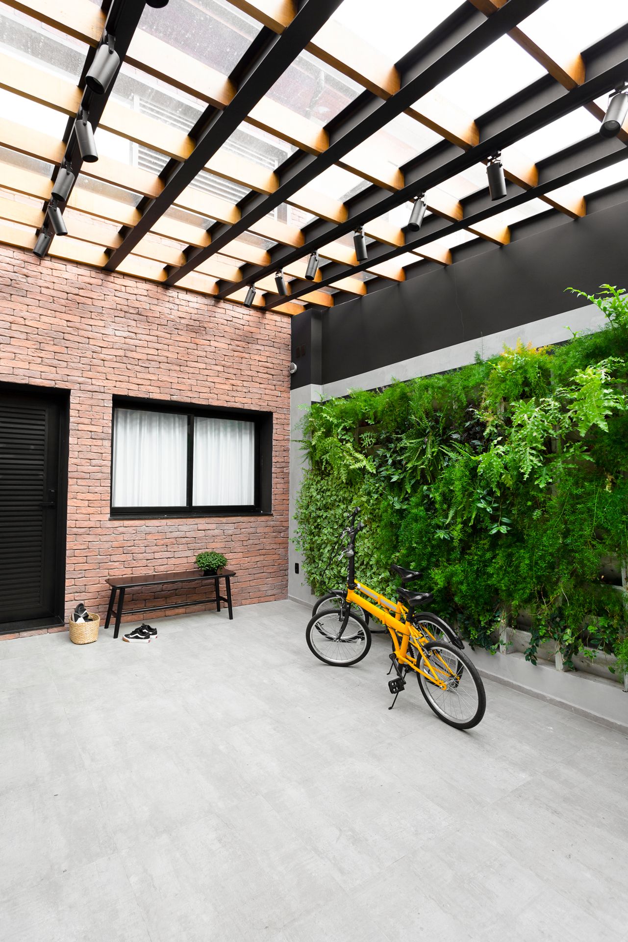 Espaço externo de casa geminada com jardim, bicicleta e cobertura metálica com vidro