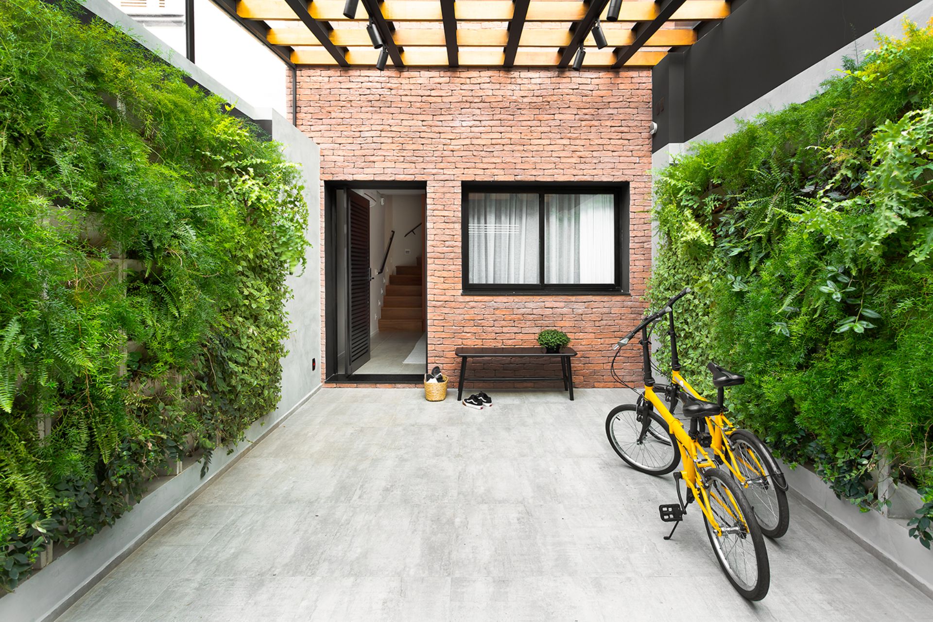 Espaço externo de casa geminada com jardim, bicicleta e cobertura metálica com vidro