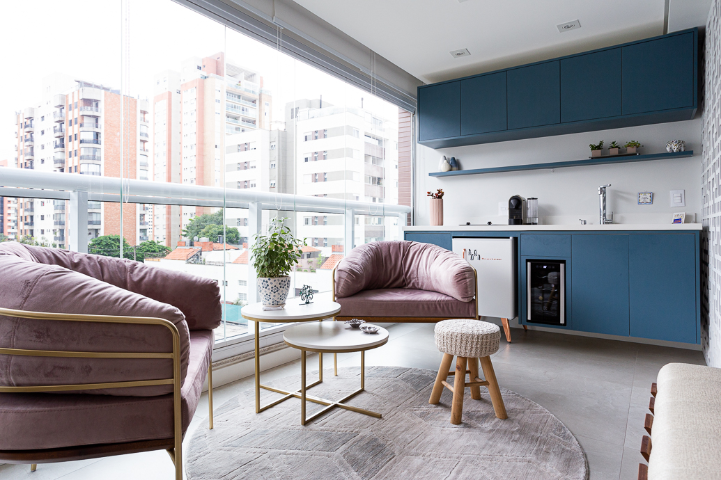 Varanda de apartamento com bancada em marcenaria azul e poltronas cor-de-rosa