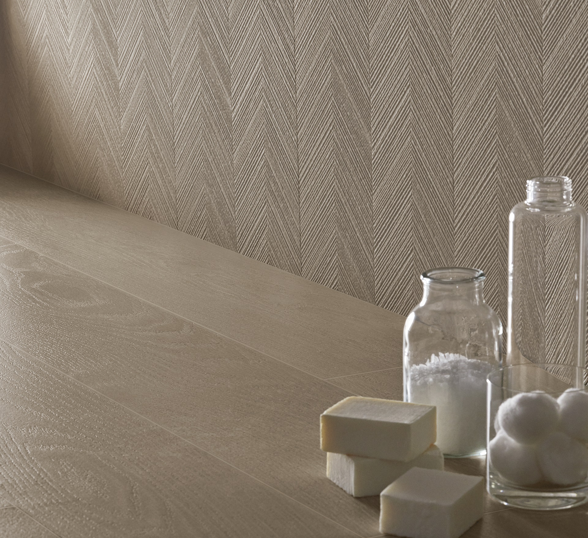 Detalhe de parede com estampa chevron texturizada. Há alguns potes de vidro e sabões na imagem