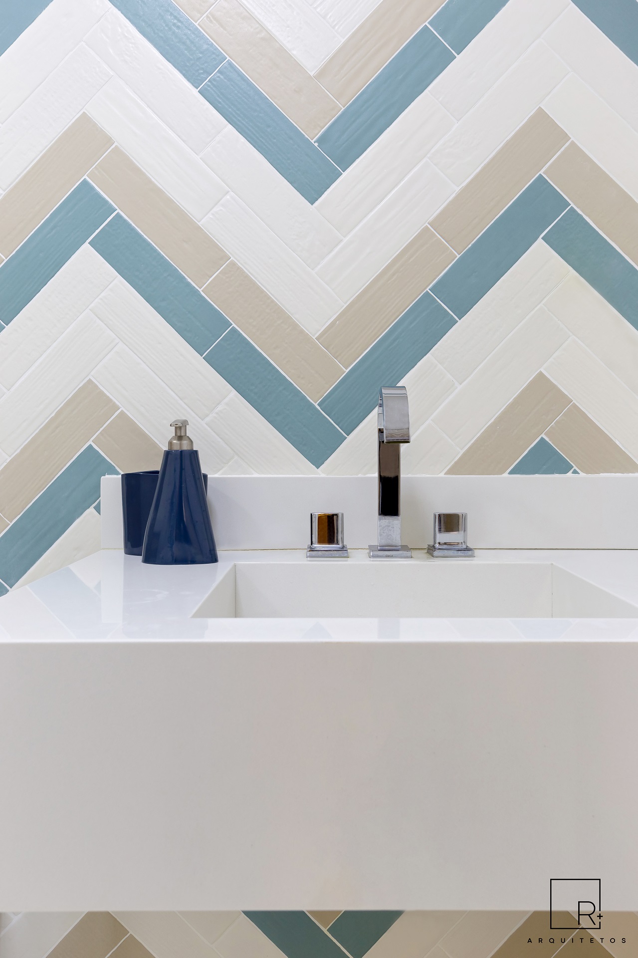 Bancada de banheiro branca. Atrás dela há uma perede revestida com uma estampa chevron em três cores: branco, amarelo e azul