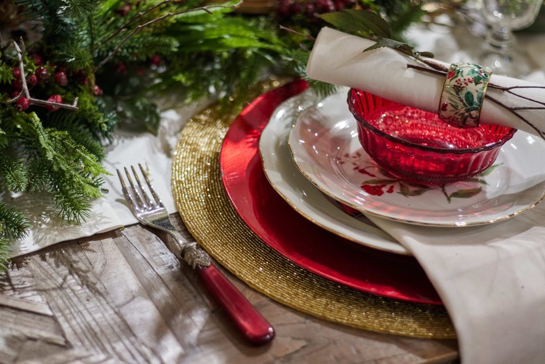 Detalhe de mesa posta de Natal, com garfo, sousplat, pratos, pote de sobremesa e guardanapo