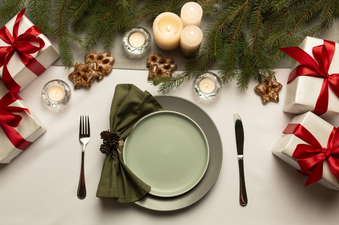 Mesa posta de Natal vista de cima, com sousplat, prato, guardanapo, talheres, velas. biscoitos, presentes e plantas