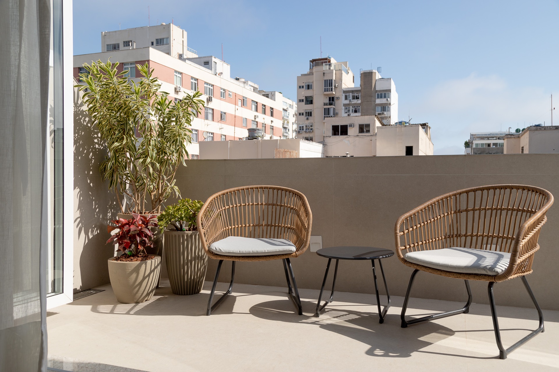 Varanda de apartamento com duas cadeiras, mesa pequena e vasos de planta, tudo com jeito de casa