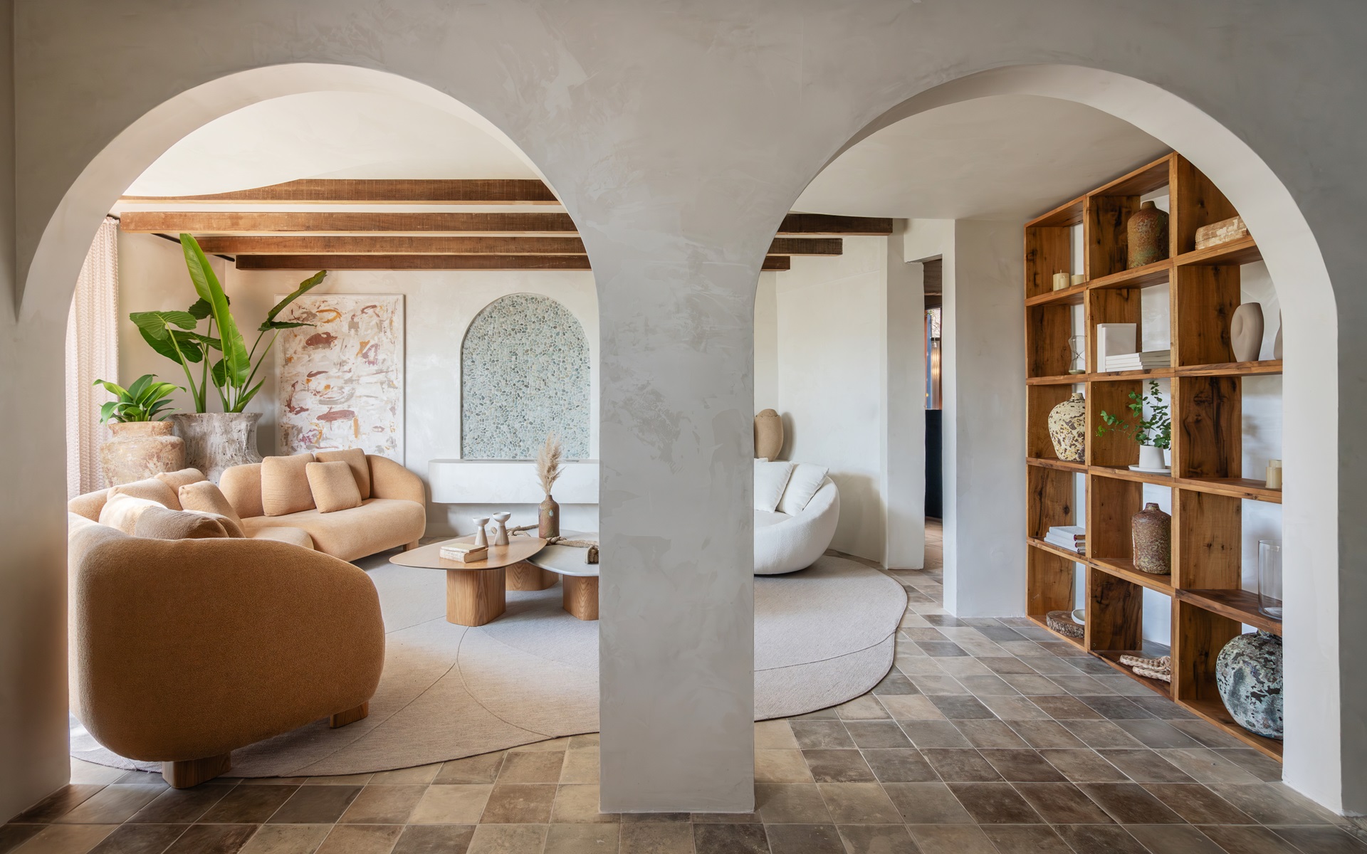 Sala em tons neutros e terrosos com dois arcos brancos na entrada