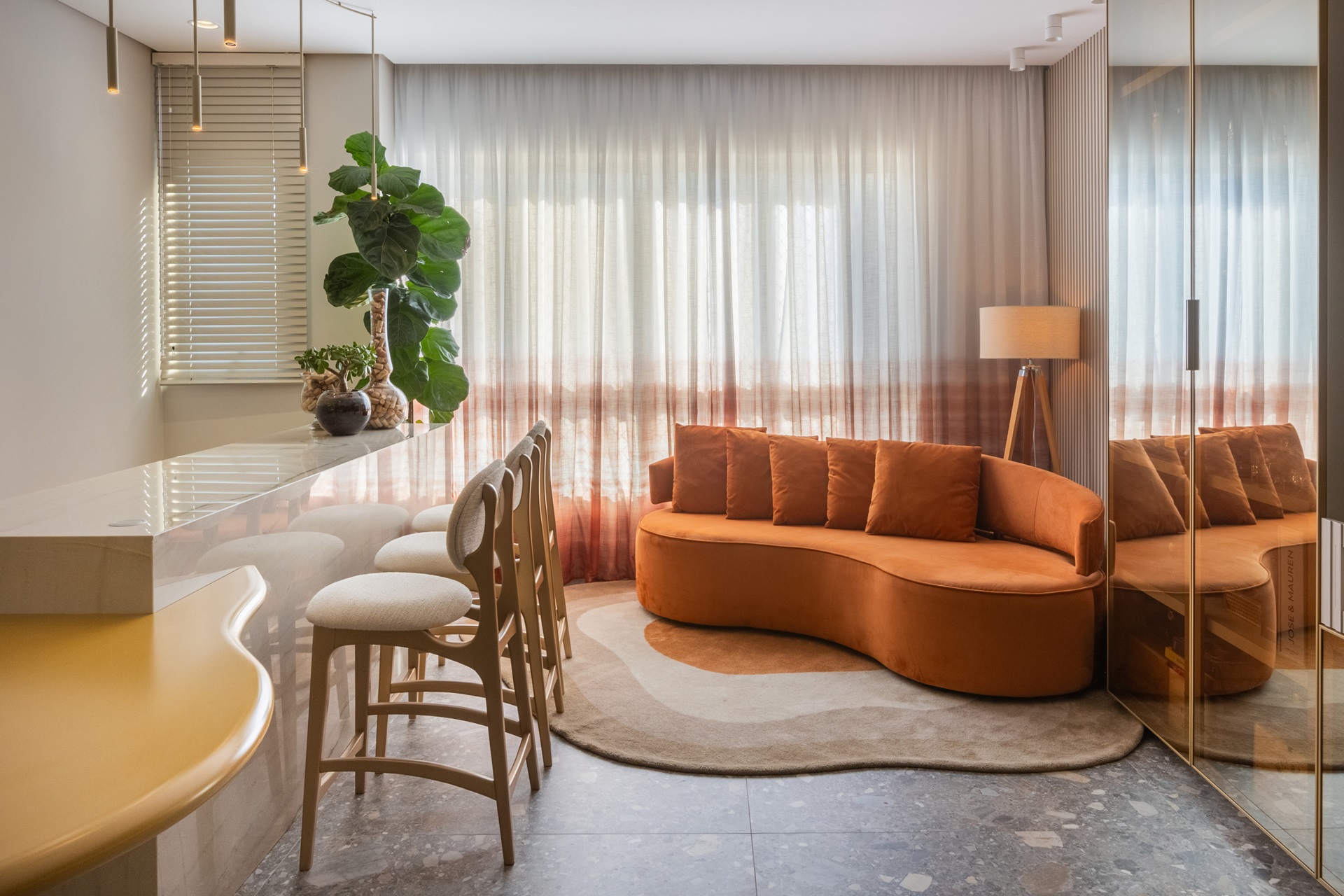 Sala integrada, com sofá laranja em forma orgânica, com tapete também orgânico abaixo do móvel